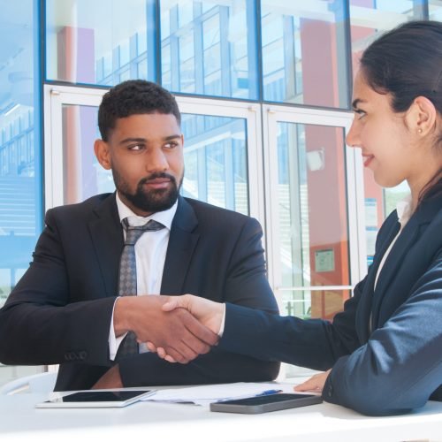 Serious business people shaking hands in outdoor cafe. Business man and woman wearing formal clothes and sitting with building glass wall in background. Deal concept.